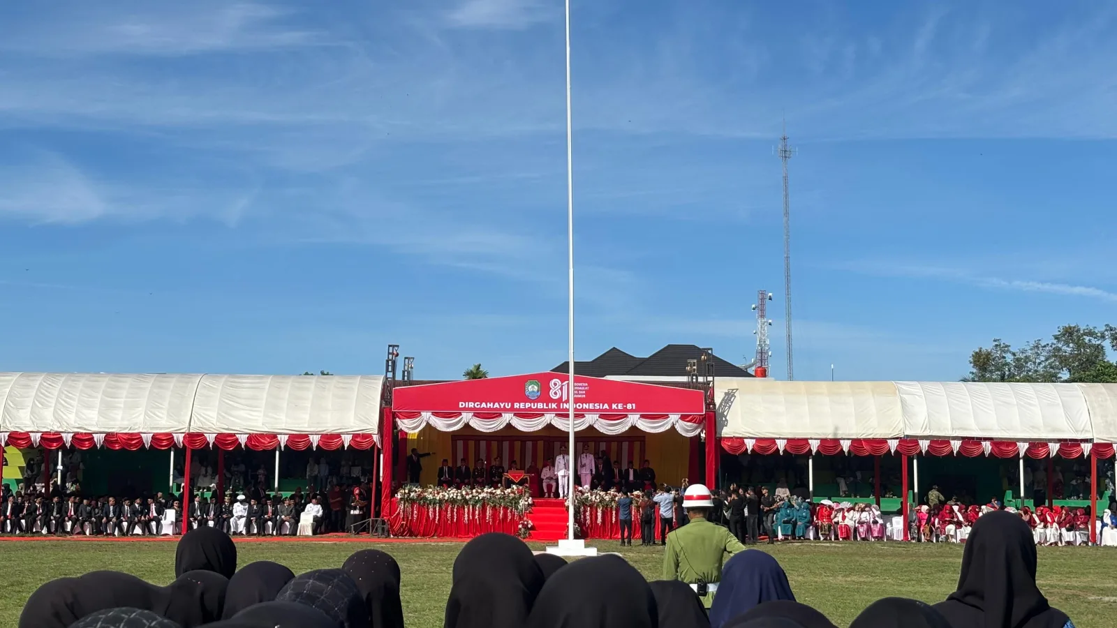 Suasana upacara pengibaran bendera HUT ke-81 RI di Lapangan Persada Blangpidie, Aceh Barat Daya, Senin 17 Agustus 2026, tampak peserta berpakaian hitam berdiri menghadap tiang bendera dan panggung utama.