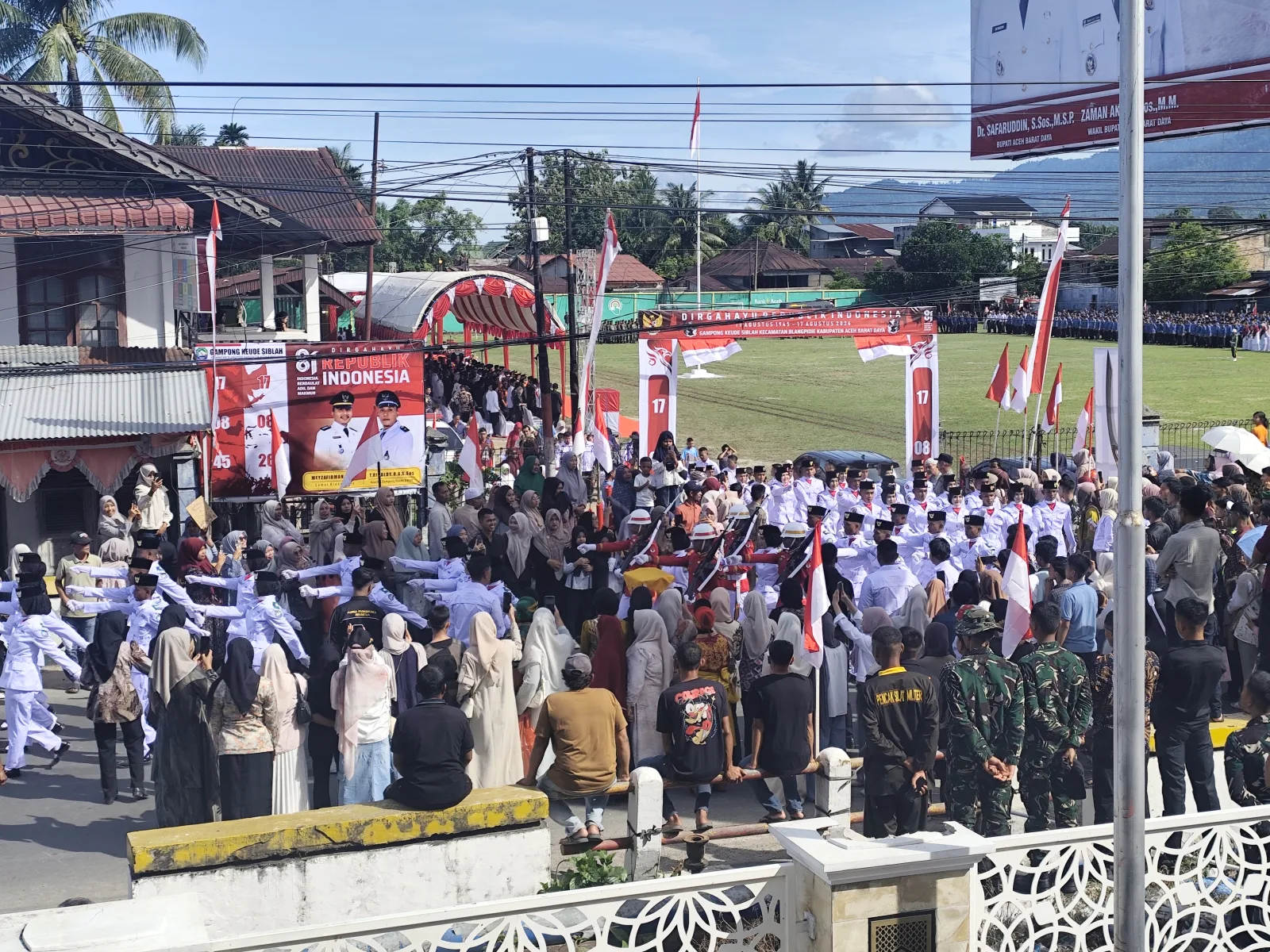 Pasukan Paskibraka berseragam putih berarak memasuki Lapangan Persada Gampong Keude Siblah, Blangpidie, Aceh Barat Daya, pada upacara HUT ke-81 RI, 17 Agustus 2026, disaksikan ribuan warga di luar pagar lapangan.